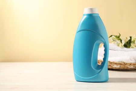 Bottle of fabric softener, terry towels and lily flowers on white wooden table against light yellow background. Space for textの写真素材