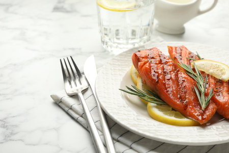 Seafood. Tasty grilled salmon served with cutlery, rosemary and lemon on white marble table, closeup. Space for textの写真素材