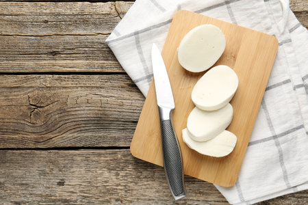 Cut mozzarella cheese and knife on wooden table, top view. Space for textの写真素材