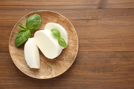 Pieces of delicious mozzarella cheese and basil leaves on wooden table, top view. Space for textの写真素材