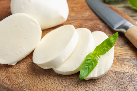 Cut mozzarella cheese with basil and knife on wooden table, closeupの写真素材