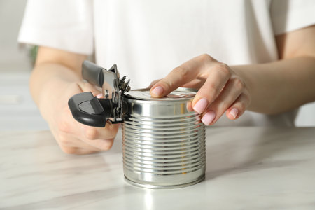 Woman opening tin with can opener at white table, closeupの写真素材