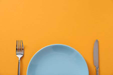 Stylish plate and cutlery on orange background, flat lay. Space for textの写真素材