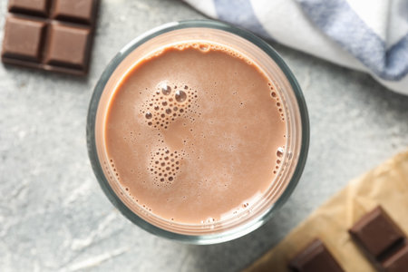 Tasty chocolate milk in glass and pieces on grey table, flat lay