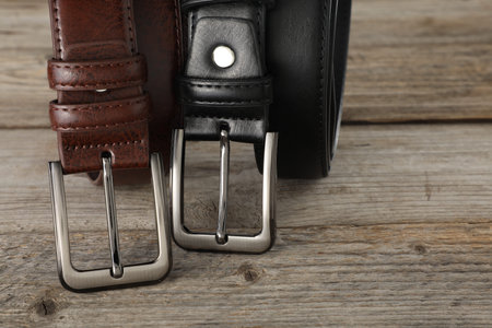 Two leather belts on wooden table, closeup. Space for text