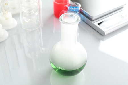 Flask with green liquid, other laboratory glassware and scale on white mirror table, closeupの写真素材