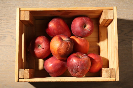 Damaged red apples in wooden crate on table, top view