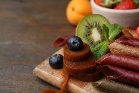 Tasty candied leather rolls, fruits and berries on wooden table, closeup. Space for textの写真素材