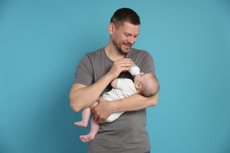Father feeding his little baby with bottle on light blue backgroundの写真素材