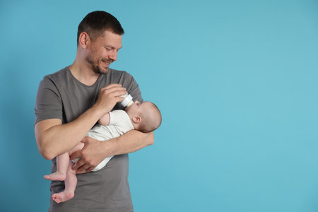 Father feeding his little baby with bottle on light blue background. Space for textの写真素材