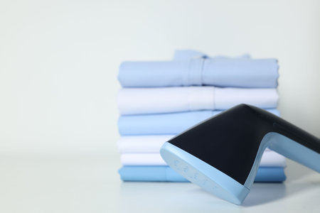 Upright steamer and stack of folded shirts on white table, closeup. Space for textの写真素材