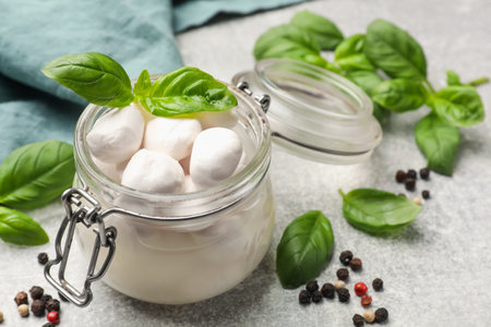 Mozzarella cheese balls with basil and peppercorns on light grey table, closeupの写真素材