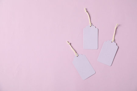 Blank tags with strings on pale violet background, flat lay. Space for text