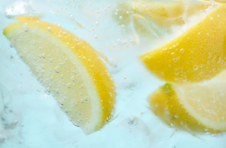 Refreshing soda water with slices of lemon and ice in glass on light blue background, closeupの写真素材