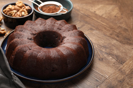 Tasty chocolate bundt cake, walnuts and cocoa powder on wooden table, closeup. Space for textの写真素材