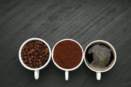 Aromatic ground coffee, beans and hot drink on black table, flat lay. Space for textの写真素材