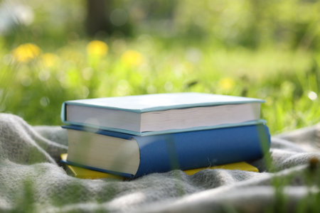 Stacked books and blanket on green grass outdoors, closeupの写真素材