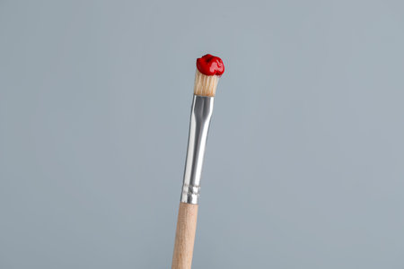 Brush with red paint on light grey background, closeup