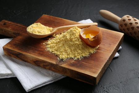 Pile of corn flour, broken egg and rolling pin on table, closeup