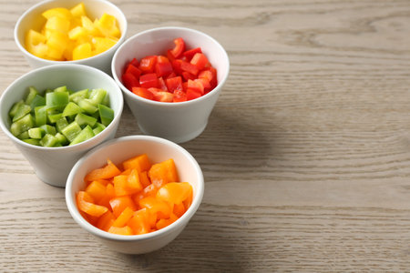 Pieces of fresh colorful bell peppers in bowls on wooden table, closeup. Space for textの写真素材