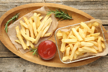 Tasty french fries served with ketchup and rosemary on wooden table, top view