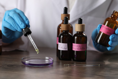 Professional perfumer developing luxury perfume at wooden table in laboratory, closeup