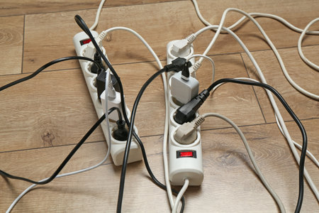 Extension power boards overloaded with plugs on wooden floor, closeup