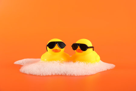 Cute rubber ducks with sunglasses and foam on orange backgroundの写真素材