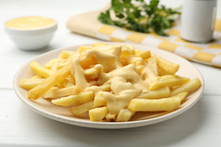 French fries with cheese sauce and parsley on white wooden table, closeup