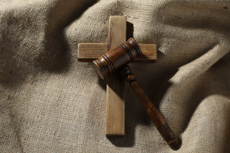 Judge's gavel and wooden cross on burlap fabric, top view
