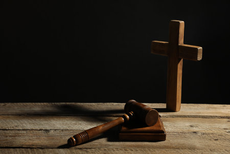 Judge's gavel and cross on wooden table against black backgroundの写真素材