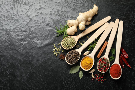 Many different spices in spoons on black table, flat lay. Space for text