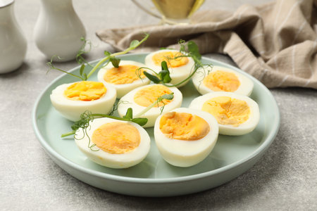 Hard boiled eggs with microgreens on grey table, closeup