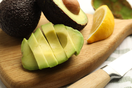 Tasty cut avocados, lemon and knife on table, closeup