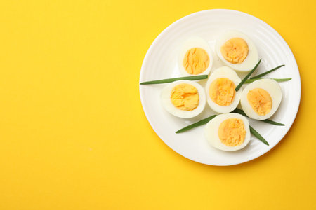 Boiled eggs and green onions on yellow background, top view. Space for text