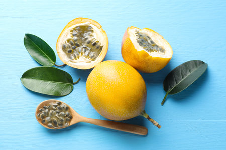 Ripe passion fruits, green leaves and seeds on light blue wooden table, flat lay