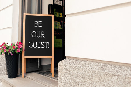 Advertising board with phrase Be Our Guest and flower pot near cafe entranceの写真素材