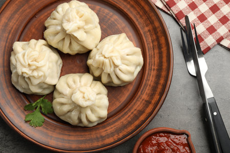 Delicious khinkali served with sauce on grey table, flat lay
