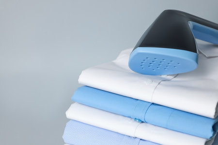Upright steamer and stack of folded shirts on grey background, closeup. Space for textの写真素材
