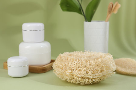 Loofah sponge and jars of cosmetic product on olive background, closeupの写真素材