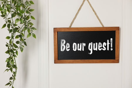 Small blackboard with phrase Be Our Guest and houseplant hanging on white wallの写真素材