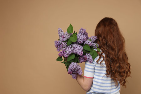 Teenage girl with bouquet of lilac flowers on beige background, back view. Space for textの写真素材