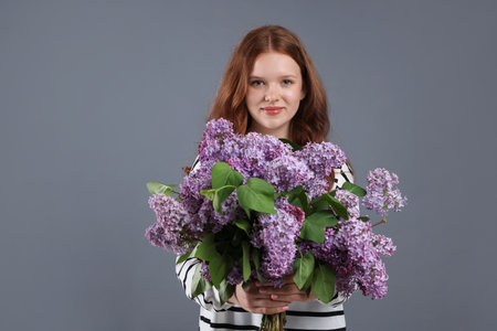 Portrait of beautiful teenage girl with lilac flowers on grey backgroundの写真素材
