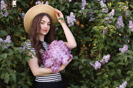 Beautiful woman among lilac flowers and leaves outdoors