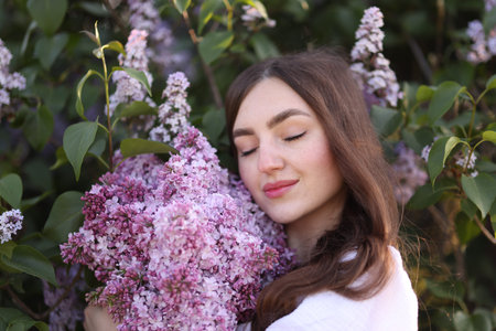 Beautiful woman among lilac flowers and leaves outdoors, closeupの写真素材