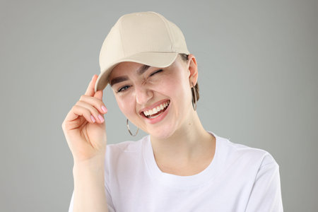 Smiling woman in stylish baseball hat on grey background, closeupの写真素材