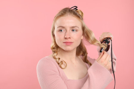Woman curling her hair on pink background. Space for textの写真素材