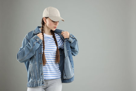 Beautiful woman in stylish baseball hat on grey background. Space for text