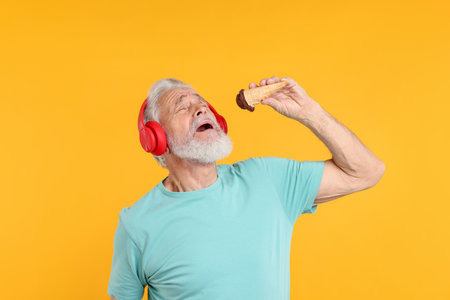 Elderly man in headphones with ice cream on orange backgroundの写真素材