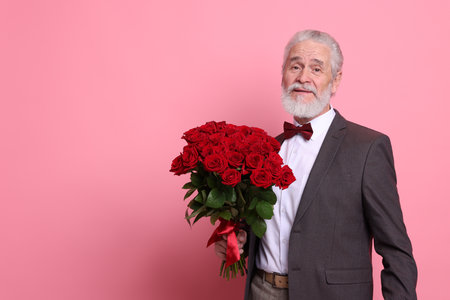 Senior man with bouquet of red roses on pink background, space for textの写真素材